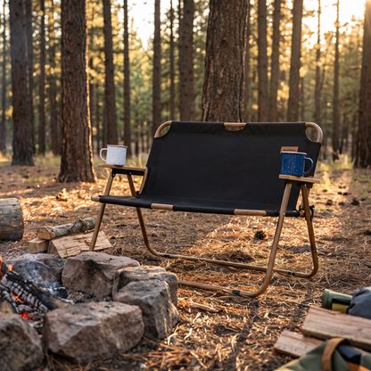 Double camping chair beside a campfire with mugs on the armrests